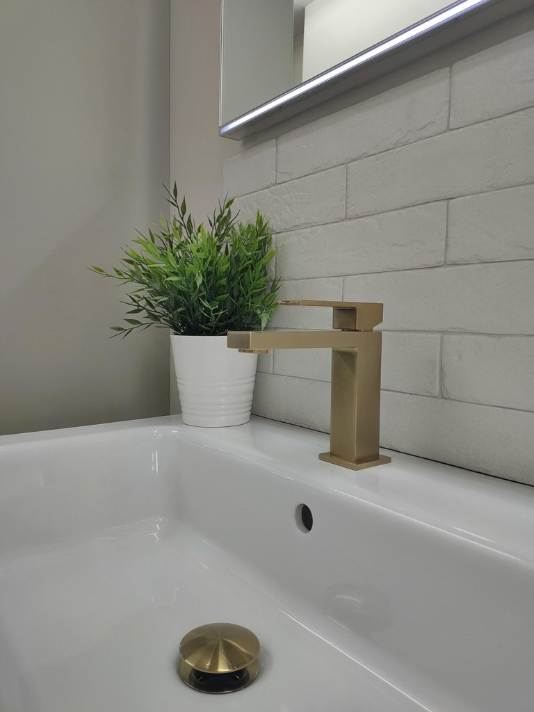 Close-up of a bathroom sink with a gold faucet and a potted plant