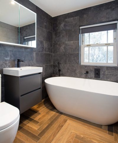Modern bathroom with a freestanding tub, black tiles, and wooden flooring