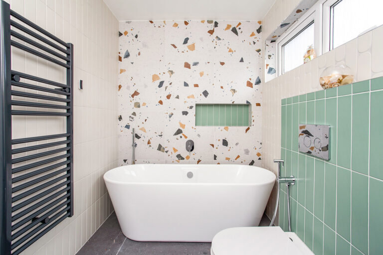 Freestanding bathtub with terrazzo tiles and a black radiator