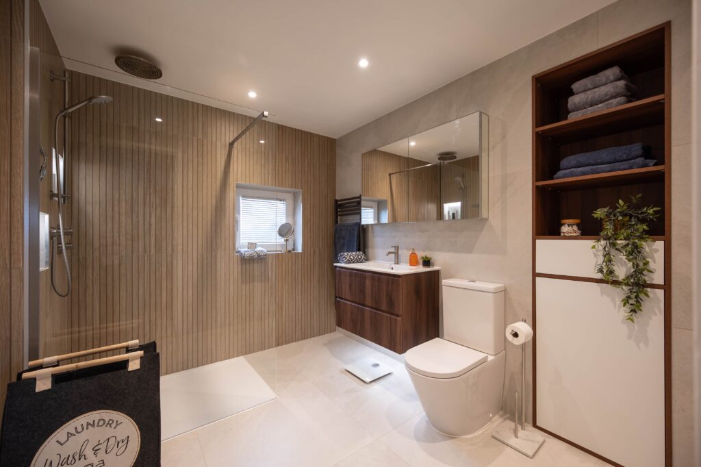 bermondsey-main-bathroom-full-view-walk-in-shower-vanity-open-shelving.jpg Full room view of Bermondsey main bathroom showing walk-in shower with glass panel and ceiling rainfall head, wall-hung walnut vanity, open shelving unit and large format neutral floor tiles