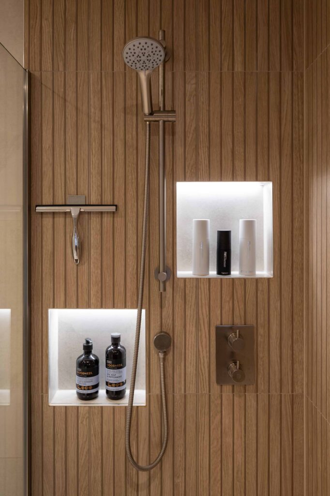 bermondsey-main-bathroom-shower-niche-brushed-steel-fittings-wood-slat-wall.jpg Detail of main bathroom walk-in shower with illuminated recessed niches, brushed steel slide rail, handheld shower and wood-effect slat wall tiling