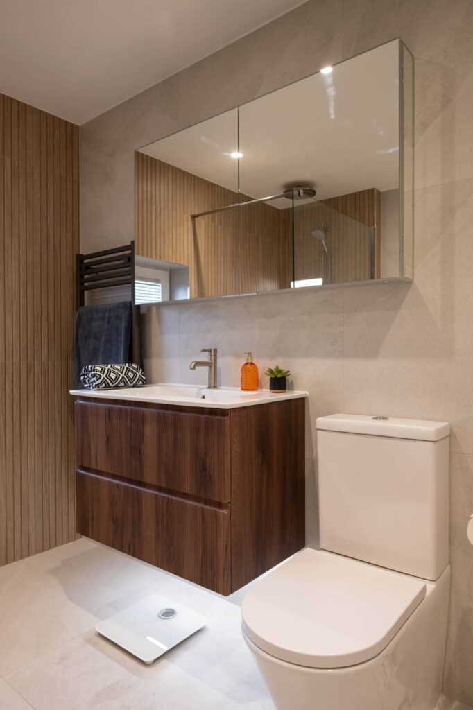 bermondsey-main-bathroom-wall-hung-vanity-mirrored-cabinet-wood-slat-feature-wall.jpg Wall-hung walnut vanity unit with integrated basin, large mirrored storage cabinet and wood-effect slat feature wall in Bermondsey main bathroom