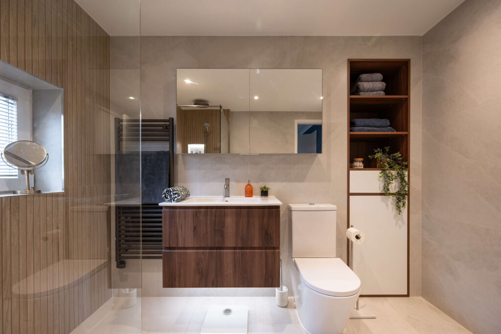 bermondsey-main-bathroom-walnut-vanity-neutral-tiles-open-shelving.jpg Warm spa-style main bathroom with walnut-effect vanity unit, large format neutral tiles, mirrored cabinet and tall open shelving unit