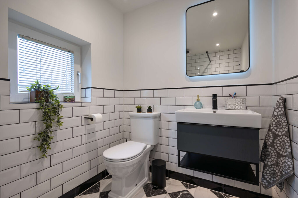 bermondsey-second-bathroom-full-view-metro-tiles-plants-vanity.jpg Wide view of second bathroom showing classic white metro tiles with black grout, monochrome diamond marble floor and dark vanity unit
