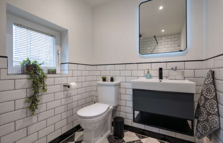 bermondsey-second-bathroom-full-view-metro-tiles-plants-vanity.jpg Wide view of second bathroom showing classic white metro tiles with black grout, monochrome diamond marble floor and dark vanity unit
