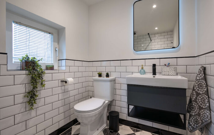 Wide view of second bathroom showing classic white metro tiles with black grout, monochrome diamond marble floor and dark vanity unit