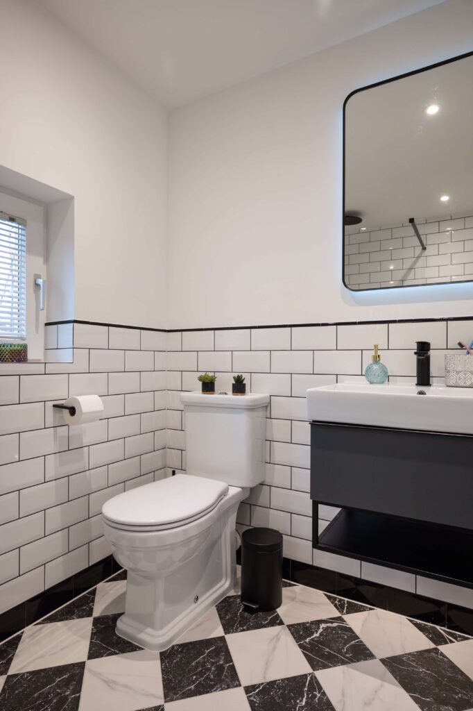 bermondsey-second-bathroom-monochrome-floor-tiles-metro-wall-tiles.jpg Full room view of second bathroom with metro tiled walls, black accents, dark vanity, illuminated mirror and trailing plant at window
