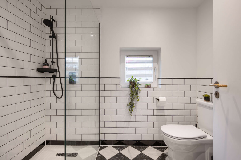 Walk-in shower enclosure with white metro tiles, black shower fittings and black grout alongside monochrome diamond floor tiles