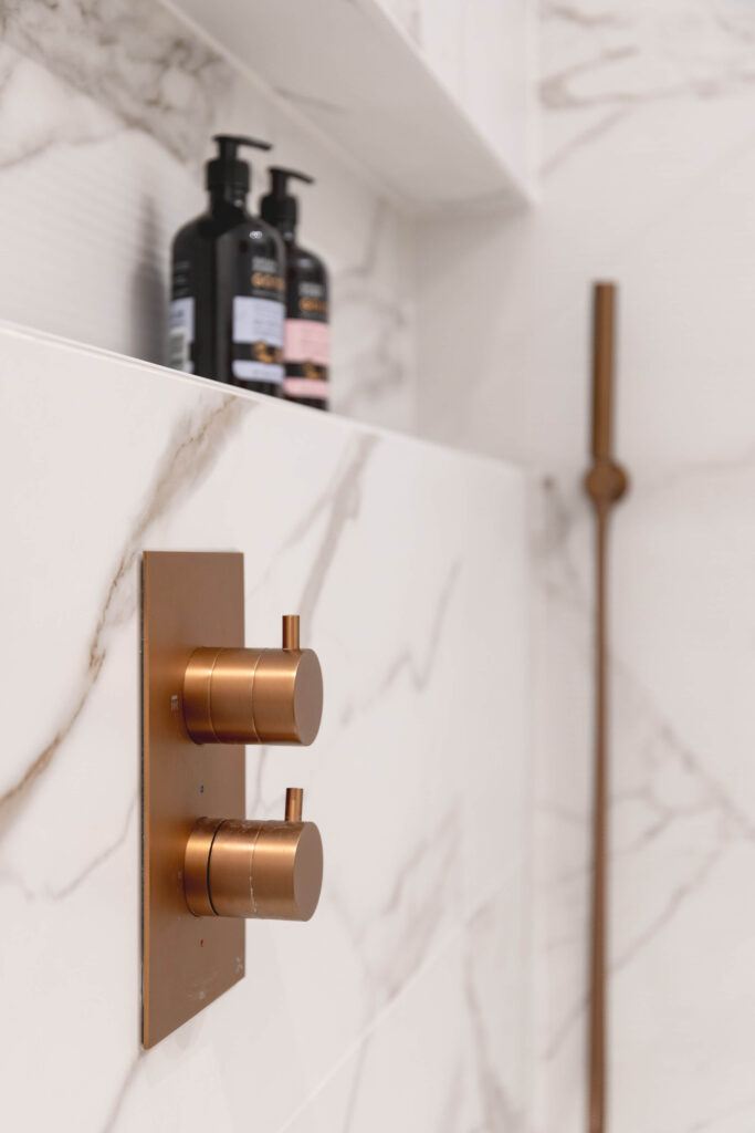 hugo-oliver-bathroom-copper-thermostatic-shower-controls-marble-closeup.jpg Close-up of brushed copper thermostatic shower controls set into marble-effect tiled wall with recessed niche and handheld shower rail beyond