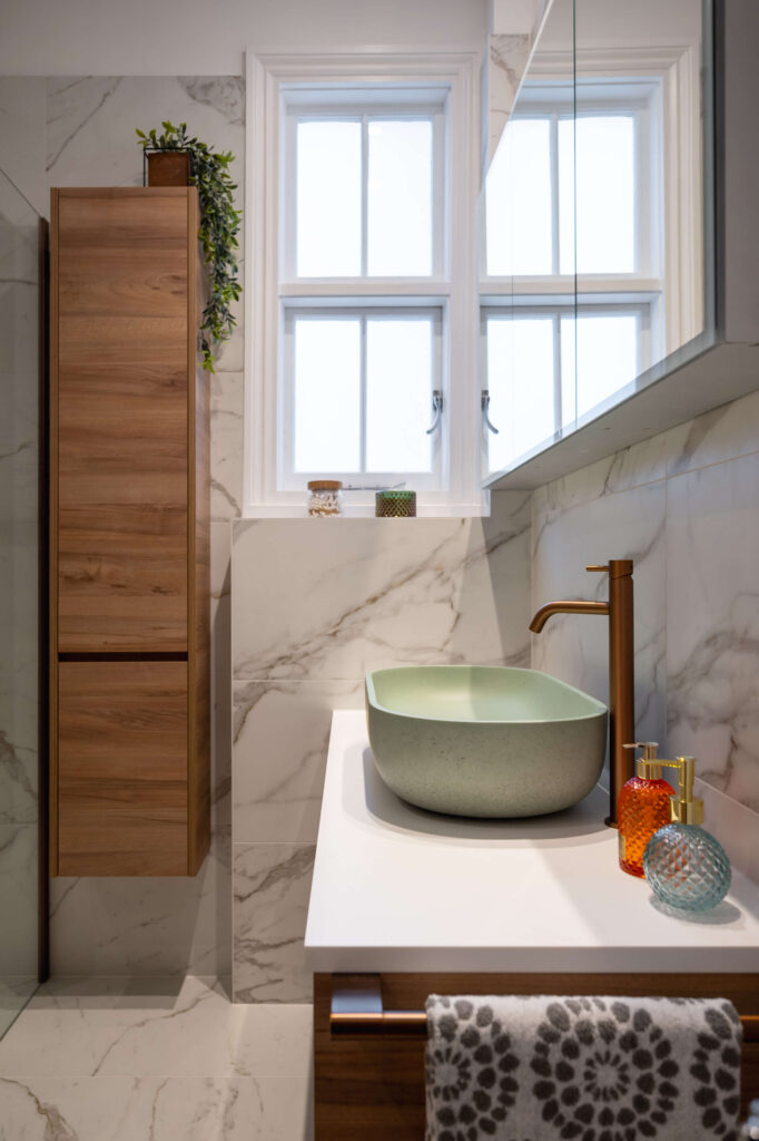 hugo-oliver-bathroom-sage-vessel-basin-copper-tap-wood-column-marble.jpg Close-up detail of wood-effect vanity drawer with brushed copper bar handle, sage green stone vessel basin and marble-effect tiled wall