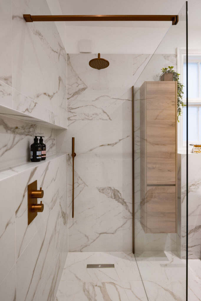 hugo-oliver-bathroom-walk-in-shower-copper-rainfall-head-recessed-niche.jpg Walk-in shower interior with ceiling-mounted copper rainfall head, copper handheld slide rail, recessed product niche and large format marble-effect tiles