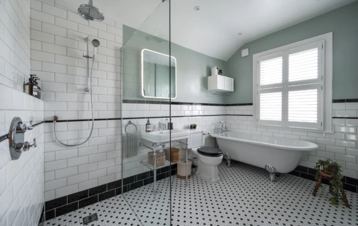 Victorian bathroom overview with freestanding bath, green cabinetry and tiled walls.